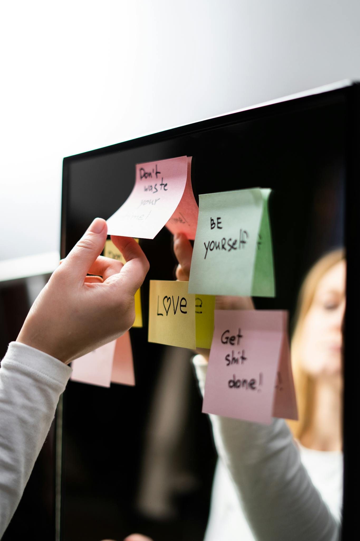 A person placing colorful motivational sticky notes on a mirror for inspiration.