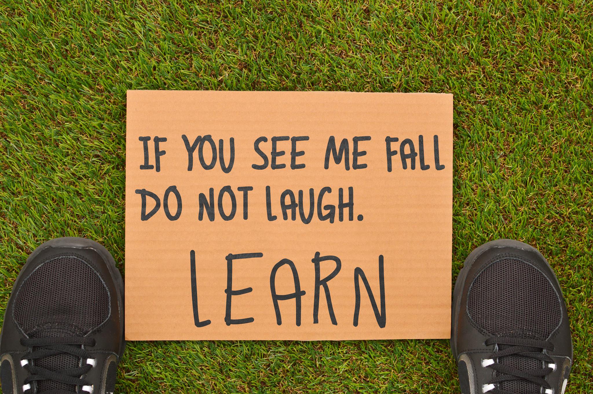 Cardboard sign with motivational message beside sneakers on green grass.